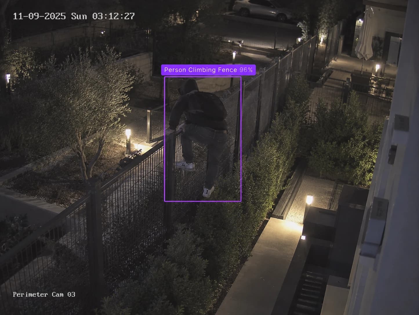 Perimeter camera at night: a hooded person climbing a fence, boxed and labelled Person Climbing Fence 96%